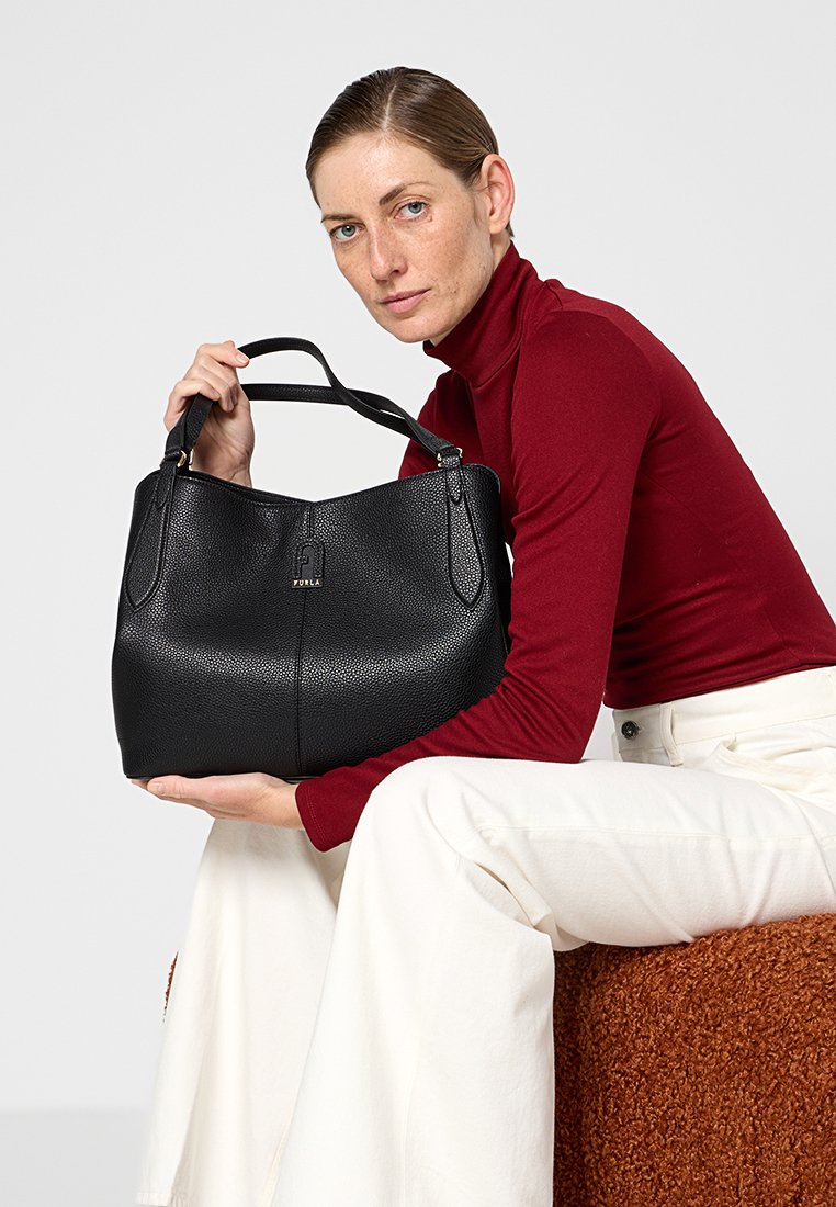 Czarna torebka z fakturowanej skóry, z podwójnymi uchwytami, w stonowanej formie oraz złotym logo. Nosi ją modelka w bordowej bluzce.