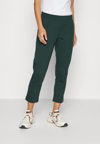 Grüne, kurze Sweatpants mit einem elastischen Bund und Seitennähten, kombiniert mit weißen und braunen Sportschuhen. Glatte Stofftextur.