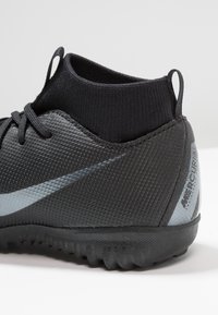 Musta urheilukenkä, jossa on teksturoitu synteettinen päällinen, elastinen nilkkakotelo ja harmaa korostusraita. Kumia oleva ulkopohja, jossa on pitoura.