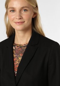 Czarna marynarka z klapami, zestawiona z przezroczystą bluzką w kwiatowy wzór o żywych kolorach. Gładki materiał i dopasowany krój.