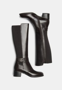 Bottes en cuir noir arrivant au genou avec une finition brillante, un panneau texturé et un petit talon. Comprend une fermeture éclair sur le côté et une sangle décorative.