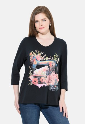 T-shirt nera con scollo a V, maniche 3/4; presenta una grafica colorata di una macchina da cucire floreale sulla parte anteriore. Tessuto morbido e elasticizzato.