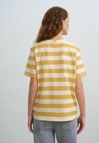 Geel en crèmewit gestreepte katoenen t-shirt met korte mouwen; beschikt over een ronde halslijn en een klein lusje aan de achterkant om op te hangen.