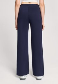 Pantaloni larghi color navy con una texture morbida, dotati di una vita elastica e di una linea dritta, abbinati a scarpe sportive grigie.