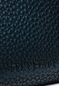 Čierna taška z texturovanej kože s vystúpeným vzorom; embosované logo "FEMESTAGE" na spodnej strane. Hladký povrch s jemným leskom.