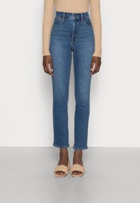 Höga blå denimjeans med smal passform, med bälteshällor och en klassisk femfickdesign, som kombineras med vävda beige sandaler.