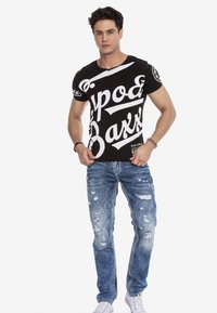Schwarzes T-Shirt mit großen weißen Buchstaben, kombiniert mit verwaschenen, blauen Jeans im Used-Look und weißen Sneakers, im Slim-Fit-Design.
