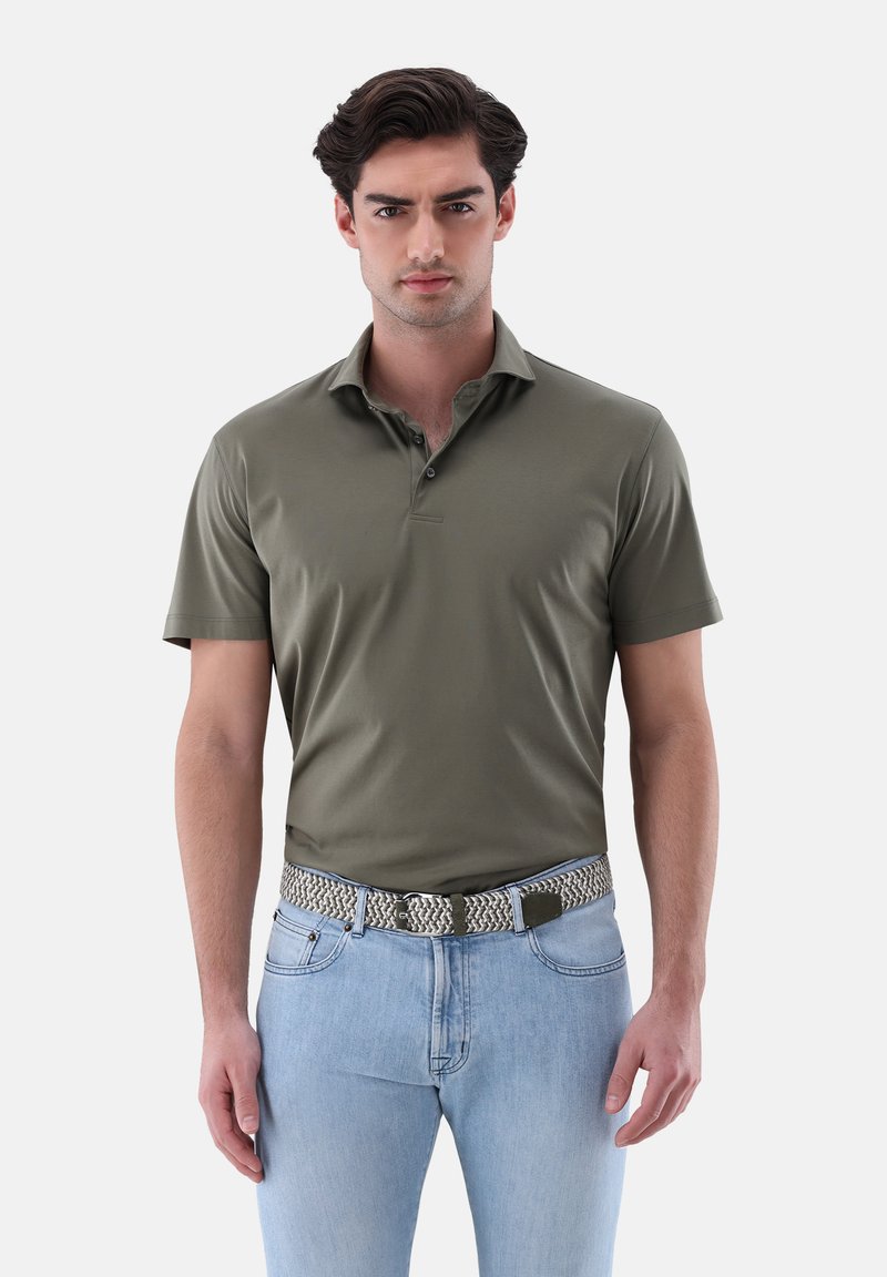 Olivgrünes Poloshirt mit umgeschlagenem Kragen, kurzen Ärmeln und einer Drei-Knopf-Leiste, kombiniert mit hellblauen Jeans und einem gemusterten Gürtel.