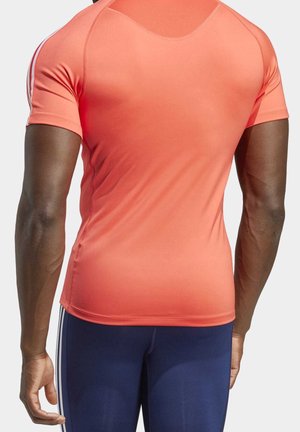 T-shirt de sport à manches courtes en corail vif, fabriqué en tissu extensible, avec des coutures plates et une coupe ajustée. Accentué par des rayures blanches.