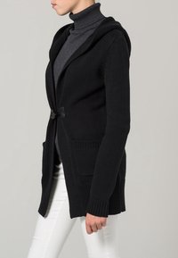 Czarny dziany kardigan z kapturem, z zapięciem na guziki, dwoma przednimi kieszeniami i ściągaczami na mankietach. Teksturowana tkanina i luźny fason.