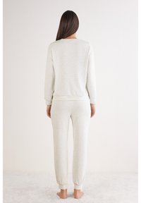 Conjunto de ropa de estar por casa de algodón gris claro que incluye una sudadera de cuello redondo y pantalones de chándal ajustados con puños elásticos. Textura suave, diseño minimalista.