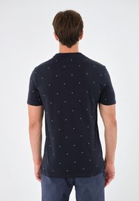 Marinblå kortärmad t-shirt med rund hals och små vita palmträdsmönster. Tillverkad av mjuk bomullstyg med en slät textur.