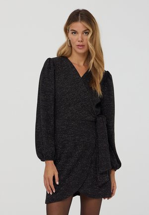 Abito nero avvolgente con maniche lunghe a sbuffo, tessuto strutturato con sottili scintillii argentati e dettaglio con cintura annodata in vita.