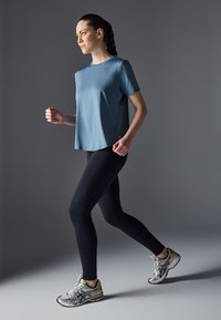 Light blue athletic t-shirt with short sleeves, paired with black leggings and silver running shoes. Smooth texture and relaxed fit.