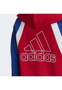 Sudadera roja, azul y blanca con una textura suave. Presenta el logo de Adidas en blanco en el pecho y una capucha con cordones.