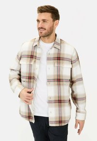 Karierte Hemd mit einem Muster aus Weiß, Beige und Braun, versehen mit roten Akzenten, kragenförmigem Design und Brusttaschen. Getragen über einem weißen T-Shirt.