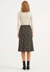 Zwarte bloemen midi-rok met een uitlopende vorm, versierd met kleine witte en beige bloemen. Glad textuur en een zoom die onder de knie eindigt.
