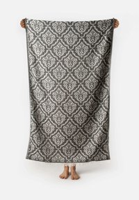 Grande coperta decorativa drappeggiata, caratterizzata da un intricato motivo damascato in argento e grigio, con un bordo frangiato per dare texture.