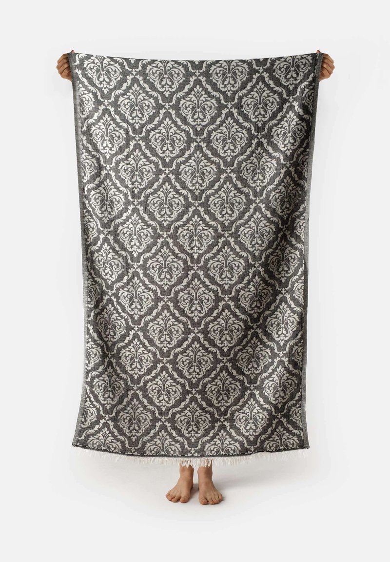 Grande coperta decorativa drappeggiata, caratterizzata da un intricato motivo damascato in argento e grigio, con un bordo frangiato per dare texture.