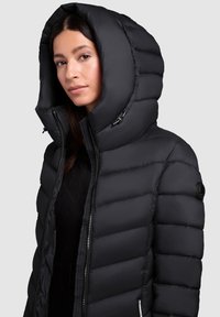 Black puffer jacket with a large hood, featuring a quilted design, zip closure, and subtle logo accent on the sleeve. Smooth texture.