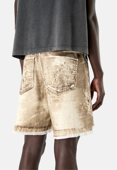 Male model wearing light beige distressed corduroy shorts with back pockets and frayed hems, paired with a loose dark gray shirt.
