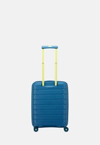 Valigia rigida blu con strisce verticali testurizzate, dotata di un manico retrattile giallo e quattro ruote multicolori.
