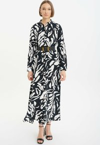 Langes Hemdkleid mit einem schwarz-weißen abstrakten Muster, ausgestattet mit einem strukturierten Kragen, langen Ärmeln und einem schwarzen Taillengürtel.