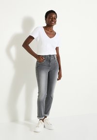 Jeans de tiro alto gris con un diseño ajustado, combinados con una camiseta blanca de cuello en V. Con detalles de bolsillos y dobladillos enrollados. Zapatillas blancas.