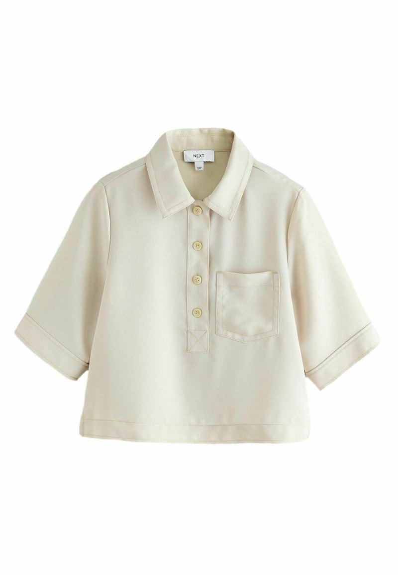 Polo de manga corta en color beige claro, con cuello plano, tapeta de botones en la parte delantera, un bolsillo en el pecho y acentos de costura sutiles.