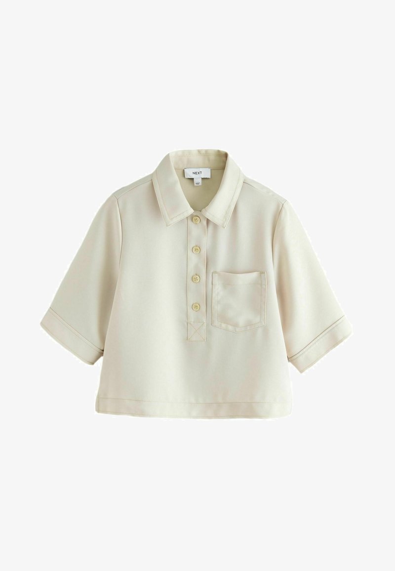 Polo de manga corta en color beige claro, con cuello plano, tapeta de botones en la parte delantera, un bolsillo en el pecho y acentos de costura sutiles.