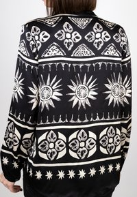 Schwarzes Stoffhemd mit weißen geometrischen Mustern, einschließlich Blumen und Sternen, mit glatter Textur und lockerer Passform.