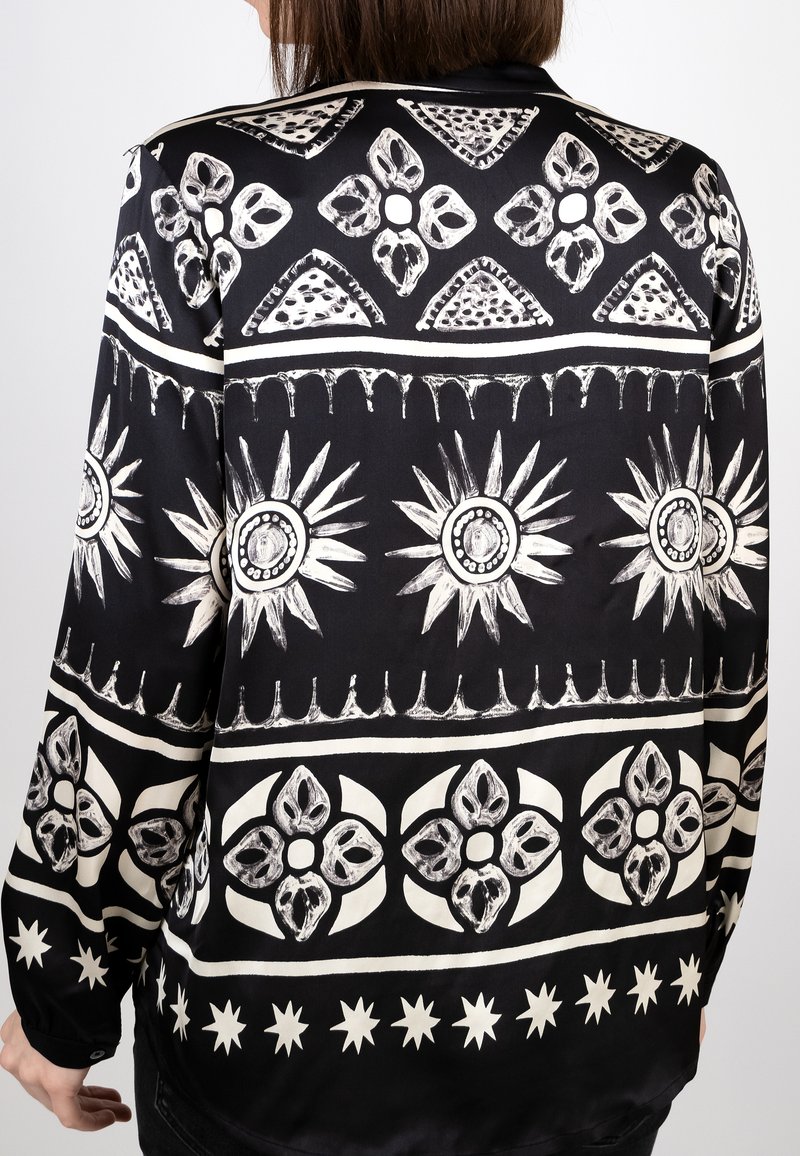 Schwarzes Stoffhemd mit weißen geometrischen Mustern, einschließlich Blumen und Sternen, mit glatter Textur und lockerer Passform.