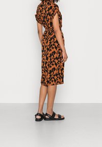 Sukienka w panterkę w kolorze pomarańczowym i czarnym, do kolan, z krótkimi rękawami i paskiem w talii. Połączona z czarnymi płaskimi sandałami.