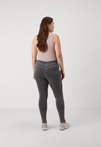 Jeans de tiro alto gris con un ajuste slim, bolsillos traseros, combinados con una camiseta sin mangas de rayas multicolores. Lleva zapatillas con detalles reflectantes.