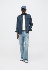 Denim shirt, light blue jeans, and gray sneakers. The shirt has two chest pockets and buttons, while the cap matches the shirt fabric.