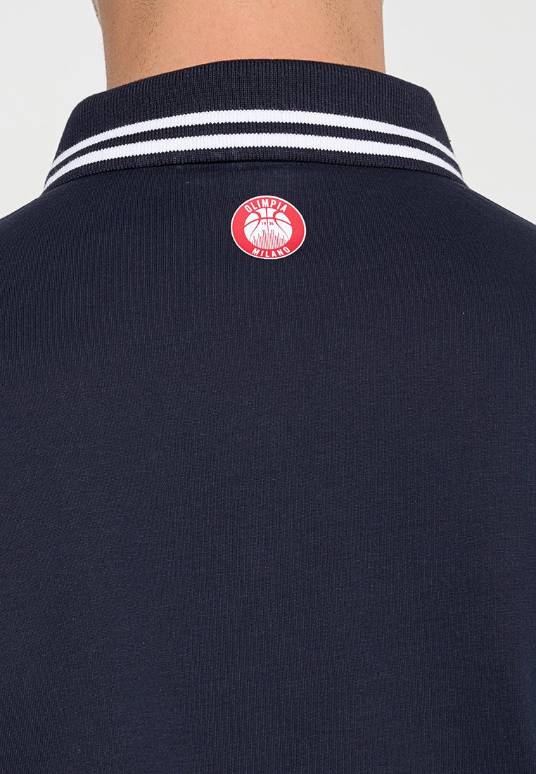 Granatowa koszulka polo z białym paskiem u kołnierza oraz okrągłym czerwonym logo z tyłu, z napisem "Olimpia Milano" i wzorem koszykarskim.