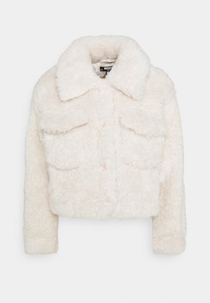 Valkoinen lyhyt keinokarvainen shearling-takki leveällä kauluksella, pitkissä hihoissa, etutaskuissa läpällä ja napituksella.
