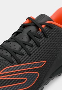 Black athletic shoe featuring a textured surface, orange accents, and black laces. The design includes a prominent logo and a cushioned collar.