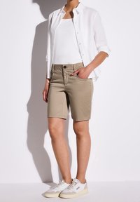 Béžové šortky délky ke kolenům s předními kapsami, doplněné bílým tílkem a lehkou bílou košilí na knoflíky. Bílé a béžové tenisky.