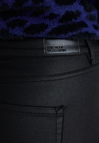 Zwarte denim jeans met een gestructureerd zwart label met de tekst "VERO MODA WE DO DENIM." Heeft een klassiek zakontwerp en een gladde afwerking.