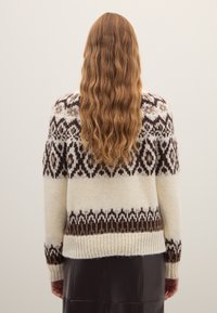 Gebreide trui met patroon in crème met donkerbruine geometrische ontwerpen, geribbelde manchetten en zoom; zachte textuur en een ontspannen pasvorm.