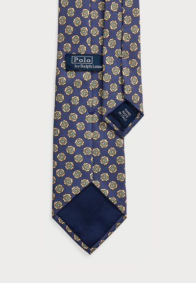 Jūros spalvos kaklaraištis su pasikartojančiu geometriniu gėlių motyvu auksinės, smėlinės ir žalios spalvos. Yra etiketė "Polo by Ralph Lauren" ir vientisas jūros spalvos galiukas.