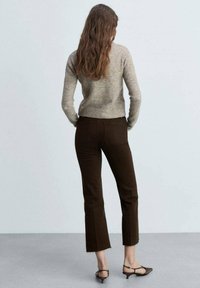 Brune flared bukser med rå kant, parret med en lys grå tætsiddende sweater. Teksturen ser blød ud, med naturligt hår der falder løst.