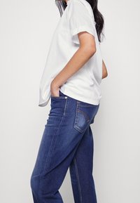 Vit kortärmad skjorta med uppvikta ärmslut, kombinerad med mörkblå denimjeans med bakficka och orange syaccenter.