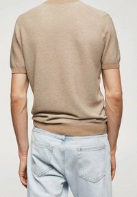 Suéter de punto beige de manga corta con textura acanalada, cintura ajustada y cuello redondo; combinado con jeans de color azul claro que tienen bolsillos traseros.