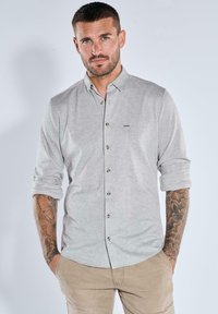 Hellgraues Hemd mit Knopfleiste und kariertem Muster, hochgekrempelten Ärmeln und braunen Knöpfen. Verfügt über eine dezente Markenkennung auf der Brust.