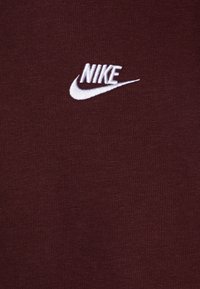 Cămașă maro, realizată din material moale, cu un logo Nike brodat alb pe față. Textură netedă, cu un design simplu.