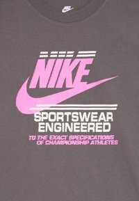Šedá látka s velkým růžovým logem Nike a textem: "Sportovní oblečení navržené podle přesných specifikací šampionů."