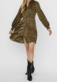 Grön mönstrad klänning med långa ärmar, krage och knäppning framtill, i kombination med svarta knähöga stövlar.