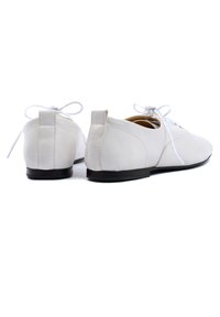 Scarpe bianche di pelle con una finitura liscia, suola nera piatta e punta rotonda. Presentano lacci, un piccolo tacco e accenti di design minimal.